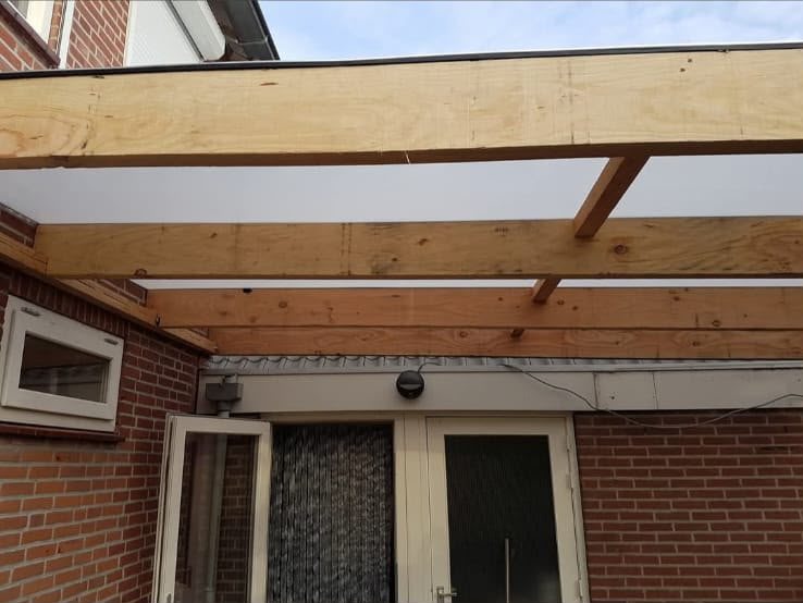 Overkapping in aanbouw met gelamineerde houten liggers tegen de gevel van de garage