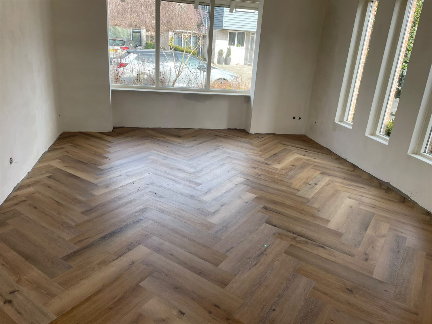 Grijsbruine visgraatvloer in een lege woonkamer met erker
