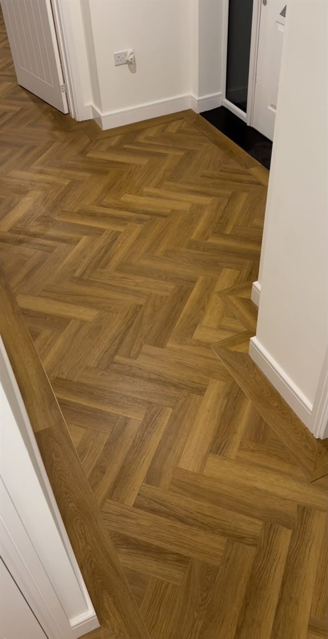 Detail van een visgraatvloer in warm eiken met strakke aansluiting op de plint